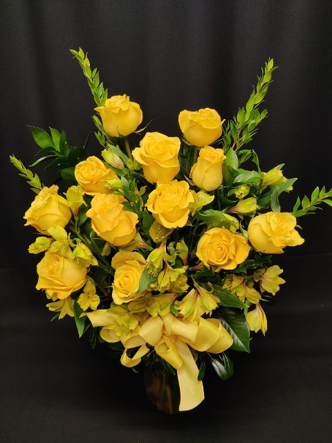 dozen yellow roses arranged in a vase with filler flowers and greens